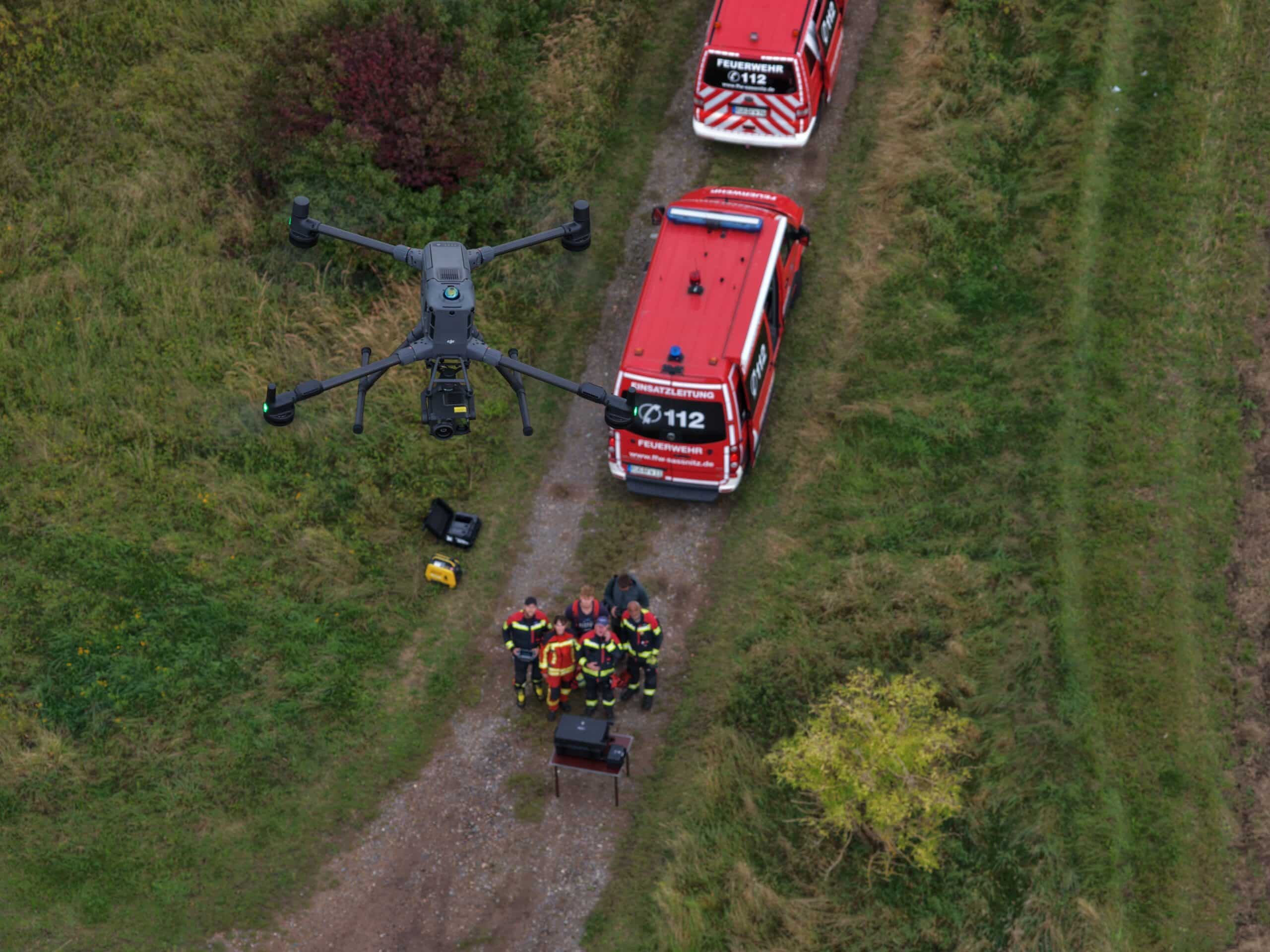 DJI Enterprise Matrice 400RTK im Feuerwehreinssatz. Die Drohne schwebt über zwei Einsatzfahrzeugen.