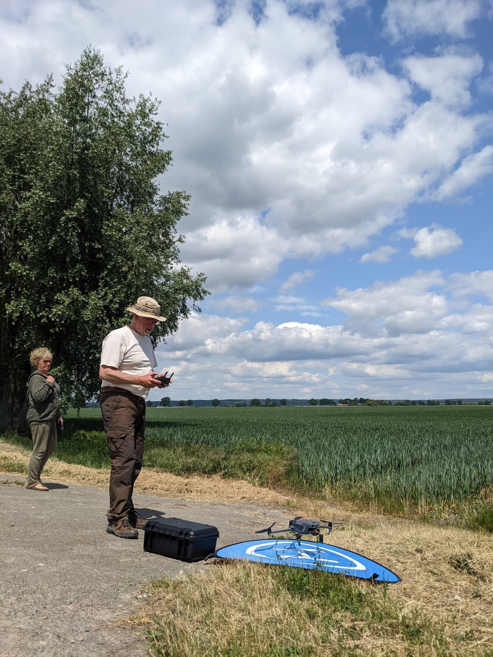 Ein Mann startet eine Drohne vor einem Feld, eine Frau schaut zu