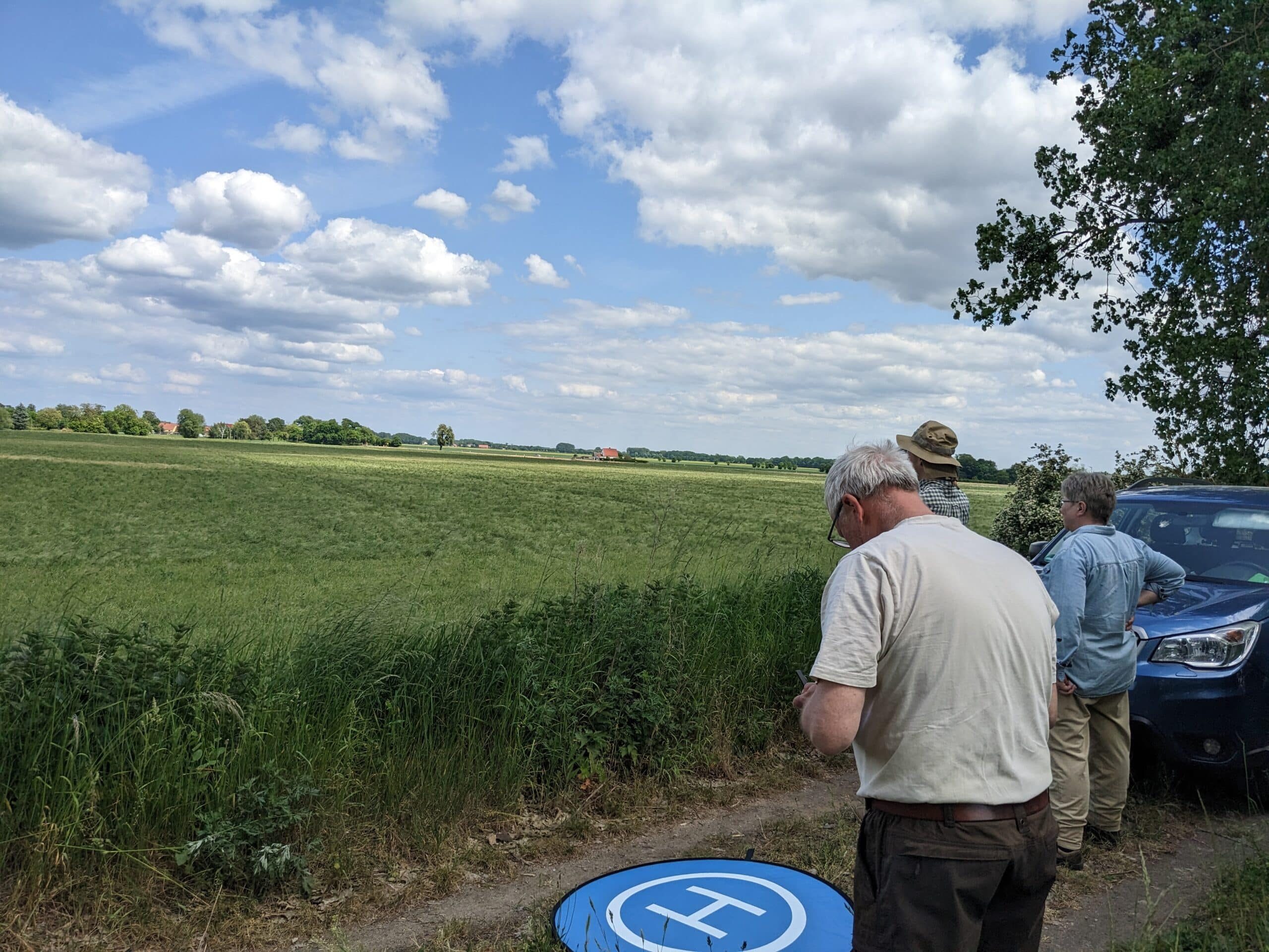 Drei Menschen stehen vor einem Feld und beobachten einen Drohnenflug