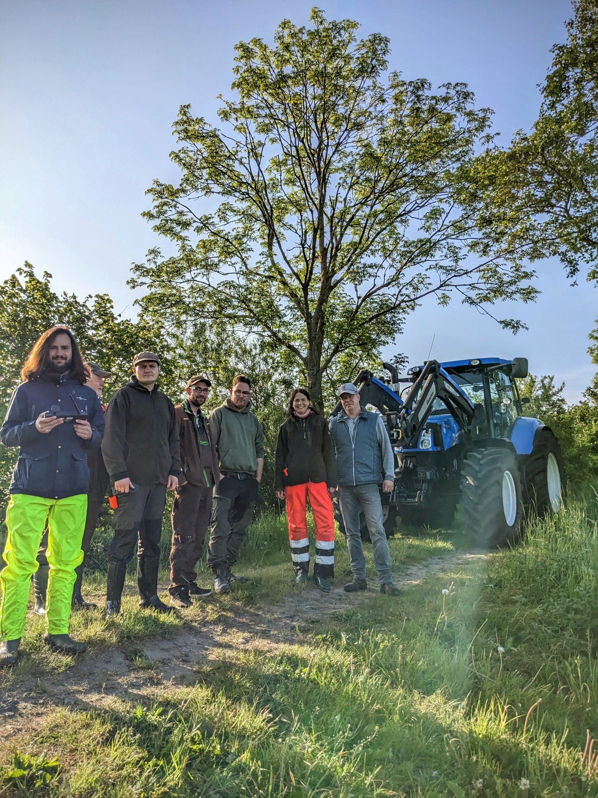Ein Team von sieben Wildtierrettern stehen auf einem Feldweg vor einem Traktor